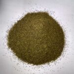 Loose green tea powder is piled into a mound on a plain white surface, with fine leaf particles scattered around the edges from Wayanad, unbranded.