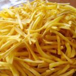Thin golden jackfruit chips pile up in a woven bowl, showing a crisp snack made from fresh raw jackfruit and fried in sunflower oil for snacking.