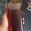 A hand holds a tall bottle of dark honey with a black cap and honeycomb texture, matching Pure medium honey-Wild and organic.