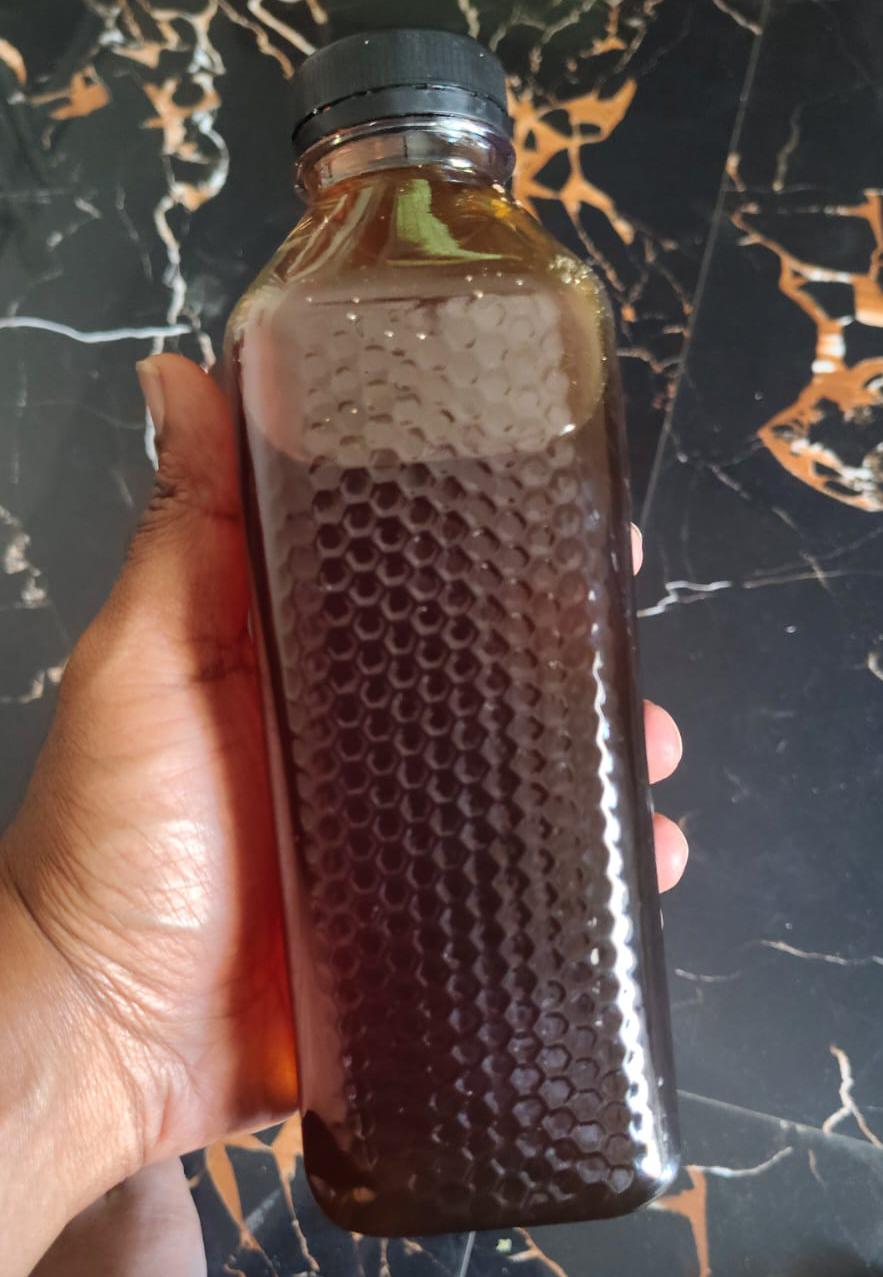 A hand holds a tall bottle of dark honey with a black cap and honeycomb texture, matching Pure medium honey-Wild and organic.